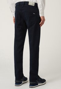 Pantaloni di cotone blu navy con taglio dritto, due tasche posteriori e un'etichetta in vita, abbinati a scarpe da ginnastica blu navy.