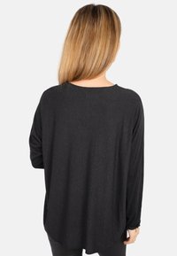 Schwarzes Langarmoberteil aus weichem Stoff, mit lockerer Passform, abgerundetem Saum und breitem Ausschnitt, mit überschnittenen Schultern.