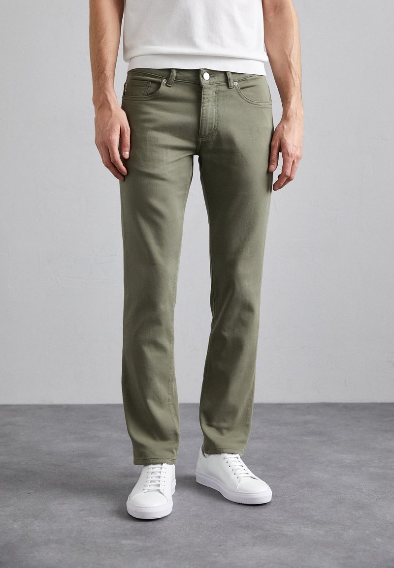 Oliwkowe spodnie z bawełny w kroju slim fit, z pięcioma kieszeniami oraz z przodem na guziki, w zestawieniu z białymi trampkami.