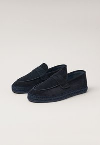 Mørkeblå ruskinds loafers med en moccasin-inspireret silhuet, der har en syet reb-sål og et dekorativt bånd henover toppen.