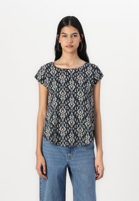 Marineblå kortermet topp med off-white blomsterdesign, rund halsutskjæring og avslappet passform, parret med lyseblå beltebukser.