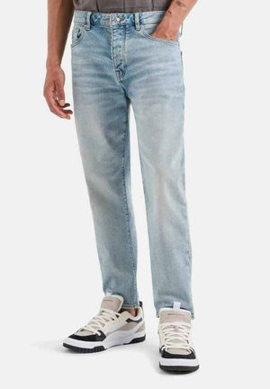 Jeans in denim azzurro chiaro con taglio dritto, leggere sfumature, design a cinque tasche, indossati con scarpe da ginnastica beige e nere.