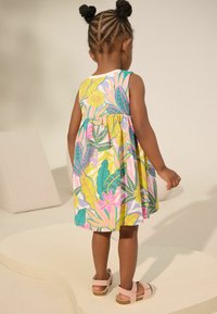 Blumenmuster-Kleid mit einem ausgestellten Rock in Gelb-, Pink- und Grüntönen. Hergestellt aus leichtem Stoff, kombiniert mit rosa Sandalen.