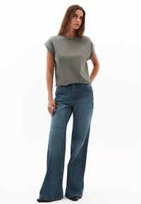 Olivengrønt cropped t-shirt med korte ærmer, parret med lyseblå vide jeans. Stoffet ser blødt ud med synlige syninger.