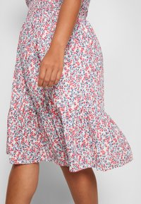 Blumenmusterkleid mit tailliertem Smock-Oberteil, fließendem Rock und farben in Off-White, Pink und Blau. Kurzer, weit auslaufender Saum mit gestuften Design.