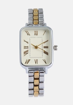 Montre rectangulaire avec un bracelet en maillons métalliques argent et or. Cadran crème avec des chiffres romains et des aiguilles couleur or, avec un marquage détaillé des secondes.
