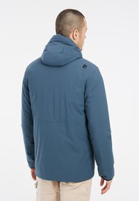 Giacca isolante blu con cappuccio. Presenta un design elegante, una texture liscia e un logo sottile sulla spalla.