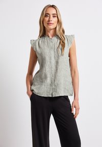 Blusa senza maniche a righe verde chiaro con chiusura a bottoni sul davanti, scollatura arricciata e tessuto morbido, abbinata a pantaloni neri a gamba larga.