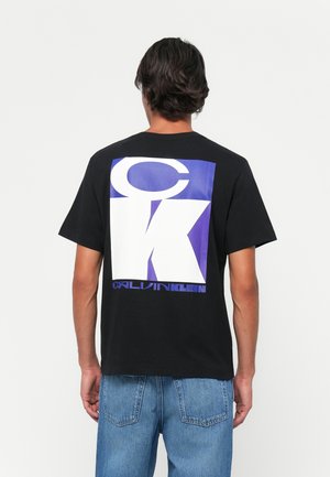 Zwarte katoenen t-shirt met een groot wit en paars grafisch ontwerp met de tekst "CK" en "CALVIN KLEIN" op de achterkant. Klassieke pasvorm.
