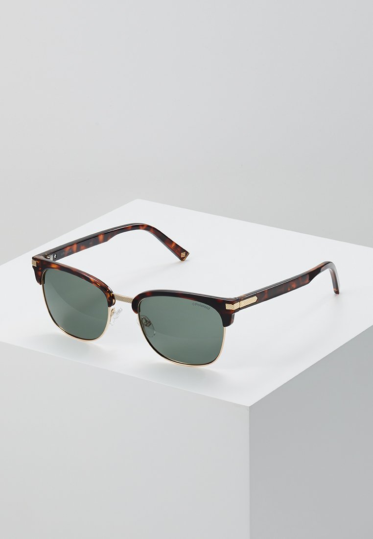 Lunettes de soleil en écaille de tortue avec verres verts et accents dorés ; forme carrée et pont en métal ; branches texturées avec détail du logo.