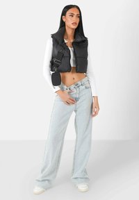 Schwarze Daunenweste mit hohem Kragen, verkürztem Design, kombiniert mit hellblauen, weiten Jeans und weißen Sneakern; beinhaltet eine kleine Umhängetasche.