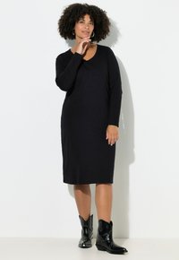 Zwarte jurk met lange mouwen en een ronde hals, gemaakt van zacht materiaal, gedragen met zwarte cowgirllaarzen, met een losse pasvorm.