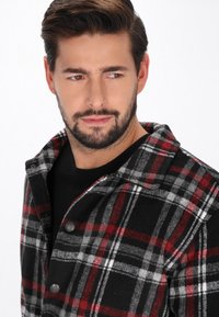 Kariertes Flanellhemd in Schwarz, Rot und Grau. Geknöpftes Design mit Kragen und weichem Material. Langärmlig, kombiniert mit einem schwarzen T-Shirt darunter.