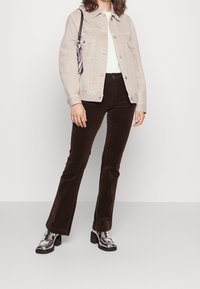 Beige denimjacka med två framfickor, matchad med mörkbruna kordfläskbyxor med utsvängd nederdel och silvriga oxfordskor. Svart handväska med ränder.