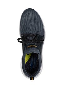 Zapatilla deportiva de color gris oscuro con una parte superior de malla texturizada, cordones negros, suela blanca y un acento amarillo en el interior de la zapatilla. Nombre de la marca "Skechers" visible.