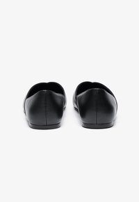 Sorte skinn ballet-flats med glatt overflate, rund tå og minimalistisk design; har en lav, flat hæl og strømlinjeformet silhuett.