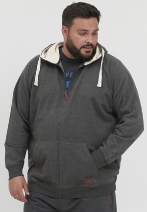 Gray zip-up hoodie with cream lining, adjustable drawstrings, front pockets, and woven label detail at the hem. Soft texture and relaxed fit.