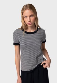 T-shirt à rayures à manches courtes avec des bordures bleu marine. Il présente un design ajusté et un tissu léger avec des rayures horizontales noires et blanches.