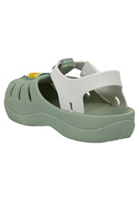 Sandalo in gomma verde con strisce bianche, dotato di fori di ventilazione, suola testurizzata e decorazioni floreali sul davanti.