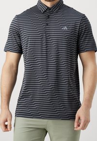 Man wearing a short-sleeve dark gray and black striped polo shirt with a collar and button placket, paired with light green pants.