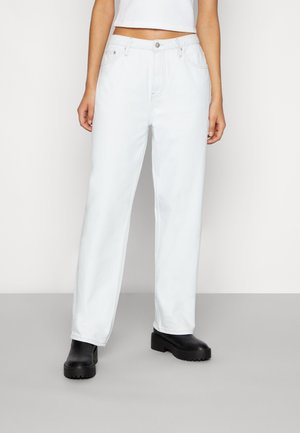 Jeans de ganga brancos com um design de perna reta, apresentando bolsos frontais, fecho de botão e costura contrastante, combinados com sapatos de plataforma pretos.