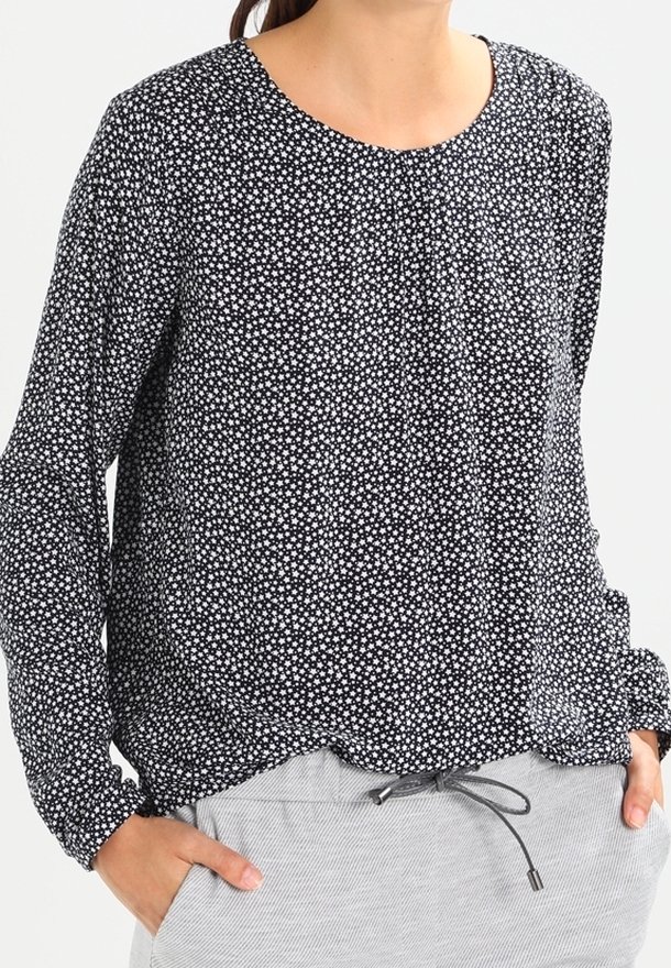 Top de manga larga en blanco y negro con pequeño estampado floral, escote redondo y fruncidos en el frente, combinado con pantalones grises con cordón.