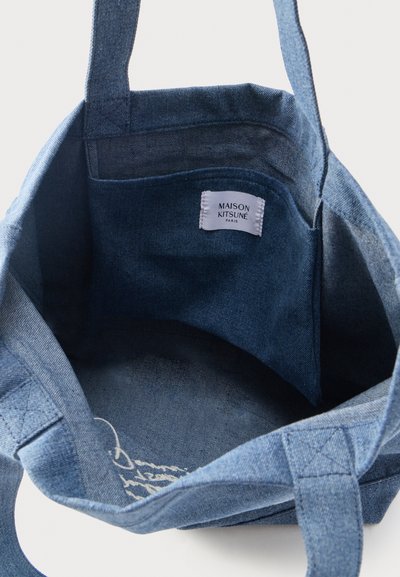 Sac fourre-tout en denim bleu avec double anses et poche intérieure étiquetée "Maison Kitsuné Paris".