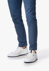 Sneakers bianchi in pelle con accenti neri, design con lacci e suola blu marina a contrasto, abbinati a pantaloni blu slim-fit.