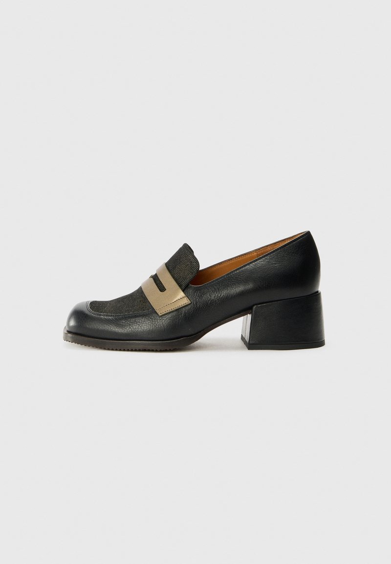 Mocassin en cuir noir à petit talon, avec une bride beige et une tige texturée, bout carré et talon bloc sur un fond gris clair uni.