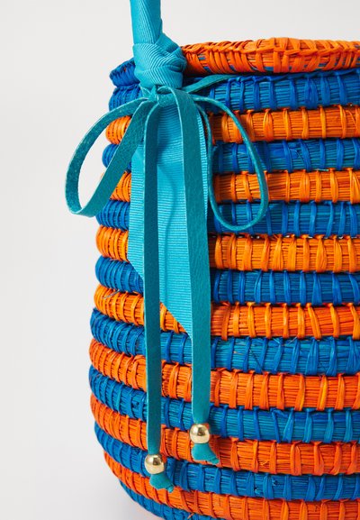Woven round basket in orange and blue with a turquoise accent ribbon and gold bead details. Features a textured, striped surface.