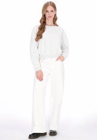 Lichtgrijze trui met ronde hals en geribde zoom, gecombineerd met witte jeans met wijde pijpen. Zwarte schoenen maken de outfit compleet.