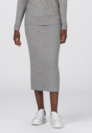 Persona vestida con una falda midi de punto acanalado gris y suéter a juego, combinados con zapatillas blancas con cordones sobre un fondo liso.