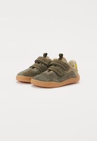 Zapatos de ante verdes con suelas de goma marrón, que cuentan con dos correas de Velcro ajustables y un pequeño acento amarillo en el talón.