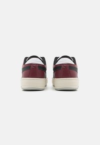 Sneaker rossi e neri con pelle texturizzata e dettagli lisci. Presentano una suola beige e dettagli in rete nera sul tallone e sulla linguetta.