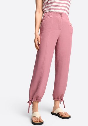 Světle růžové, lehké kalhoty s uvolněným střihem, stažení na manžetách a dvěma předními kapsami, v kombinaci s béžovými sandály.