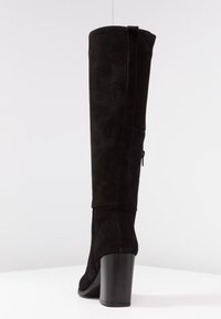 Bottes en daim noir au-dessus du genou avec un talon carré. Elles présentent une fermeture éclair sur le côté et des détails de couture à l'arrière. Texture lisse, design tall.