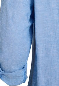 Približni prikaz zarolanog dugog rukava na svijetloplavoj tkanini košulje, prikazujući teksturu tkanine i detalje šavova na manžeti.