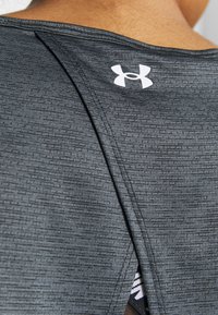 Svart sporttopp med texturerat material, med en liten slits bak och en vit Under Armour-logga på övre delen av ryggen.