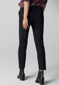 Pantalon navy à coupe slim, avec une bande latérale rouge contrastante. Texture lisse et taille mi-haute, associé à des bottines noires.