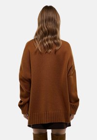 Pull marron surdimensionné avec un ourlet et des poignets côtelés, présentant un motif de tricot texturé. Le design a une coupe décontractée et des épaules tombantes.