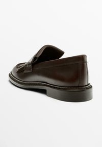 Mocassins en cuir marron avec languette en V et détail décoratif à pompon. Bout arrondi, semelle texturée et coutures apparentes.