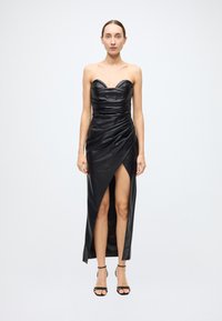 Black leather strapless dress with a sweetheart neckline, ruched detailing, and a thigh-high slit. Paired with black strappy sandals.