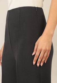 Pantalons noirs taille haute en tissu lisse, dotés d'une fermeture éclair sur le côté, d'une coupe droite et de détails de couture à l'avant.