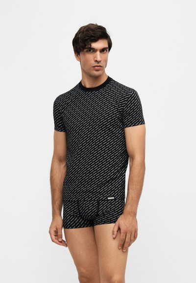 Jeune homme portant un t-shirt noir ajusté à manches courtes et un boxer assorti avec un motif à rayures blanches en diagonale sur un fond uni.