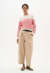 Stickad tröja med röda ränder på en krämfärgad bakgrund, kombinerad med beige vida byxor och grå slip-on skor. Svart bälte ingår.