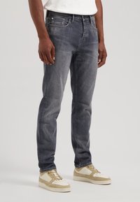 Jeans slim-fit de culoare gri închis, cu un ușor efect de uzură, design cu cinci buzunare și accesorii metalice; asortate cu adidași de culore deschisă.