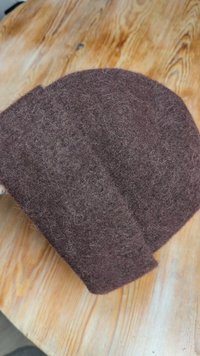 Brown felt cap with a soft, textured surface and rounded shape; features a double-layered design with an overlapping section.