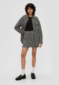 Grijs en zwart textuurjacket met twee voorzakken, gecombineerd met een zwart top en een bijpassende rok. Zwarte loafers en witte sokken.
