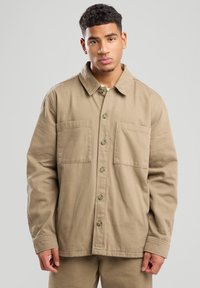 Giacca di cotone beige con colletto, due tasche frontali e chiusura a bottoni. Caratterizzata da una vestibilità rilassata e un tessuto testurizzato.