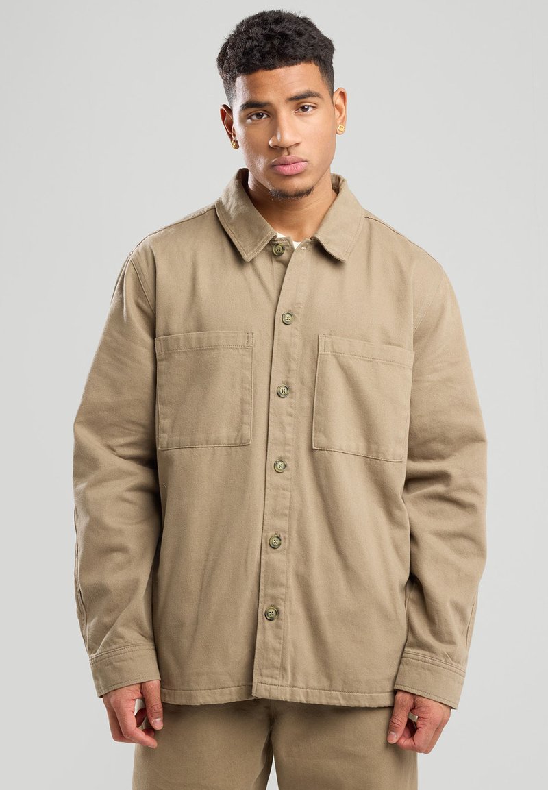 Giacca di cotone beige con colletto, due tasche frontali e chiusura a bottoni. Caratterizzata da una vestibilità rilassata e un tessuto testurizzato.